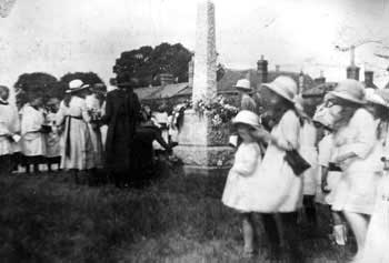 Girls in white dresses and hats gathered around the war memorial at its dedication