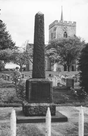 The war memorial, a tall granite column on a square base, in St Mary's churchyard with the church tower behind